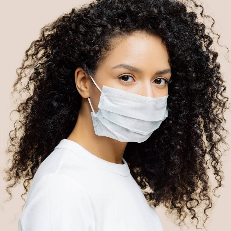 Photo of light skinned Afro American woman with curly bushy hair, wearing protective face mask.