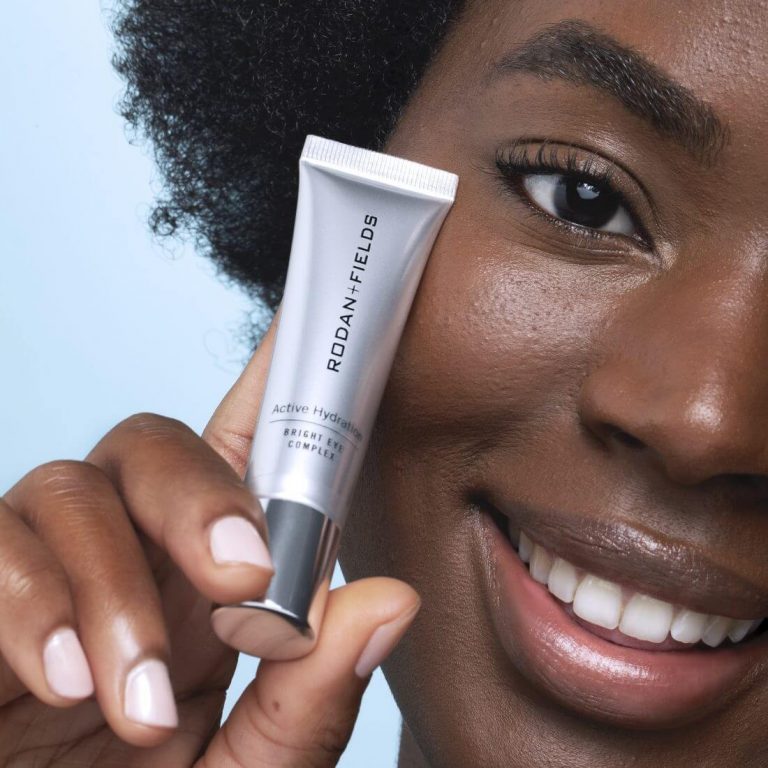 Closeup of woman with dark skin holding Rodan + Fields Bright Eye Complex