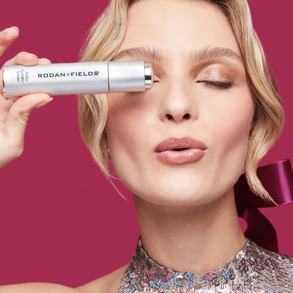 Woman with eyes closed holding a bottle of Rodan + Fields Active Hydration Serum in front of one eye
