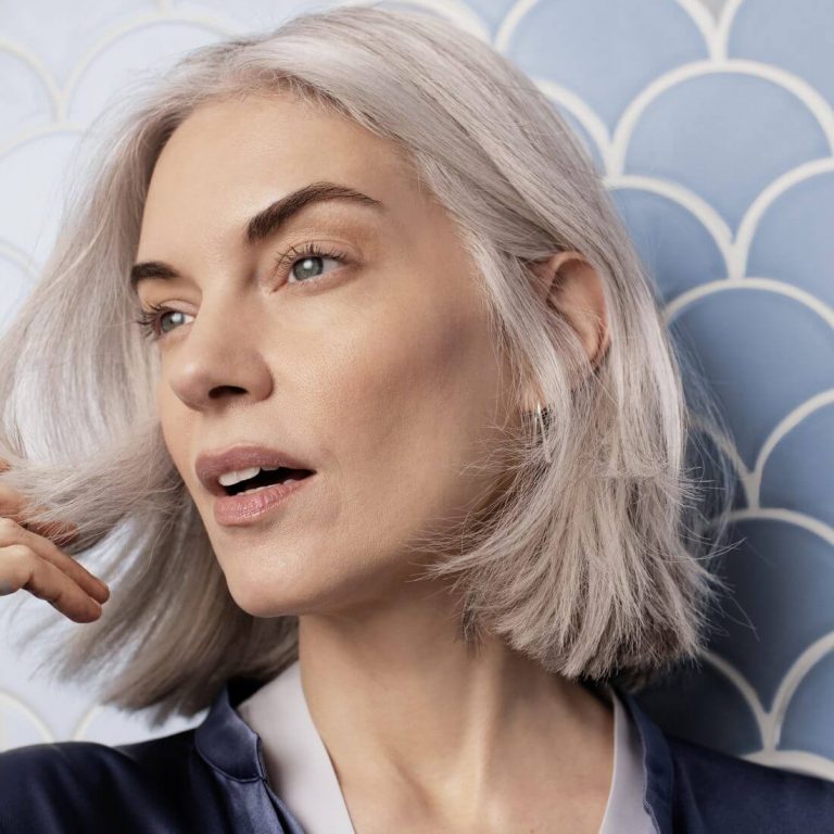 Woman with grey hair and smooth skin against a tiled wall