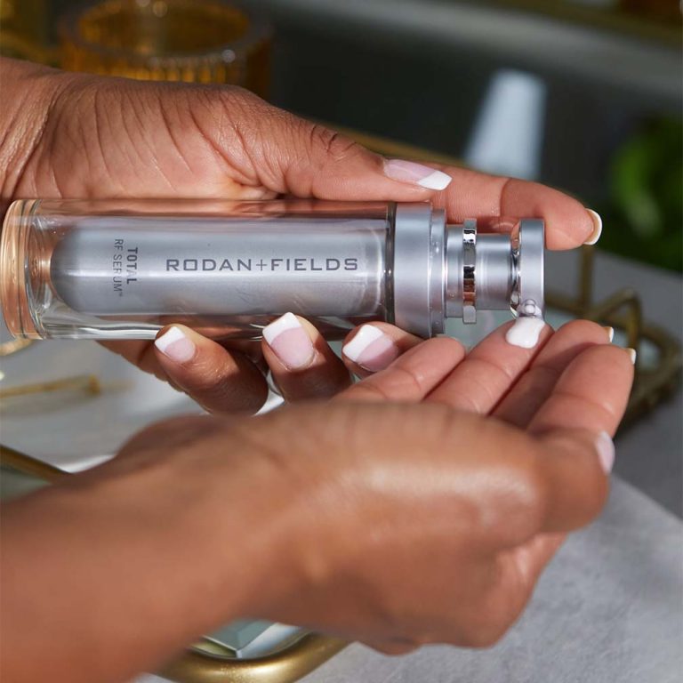 Woman dispensing Rodan + Fields Total RF Serum to her hand at a bathroom sink.