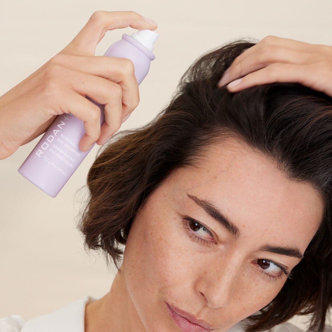 Woman with dark hair applying Rodan + Fields Refresh+ Dry Shampoo