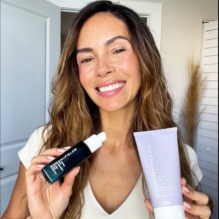Woman spiling for the camera, holding Rodan + Fields Define Curl Cream and Defrizz Oil Treatment