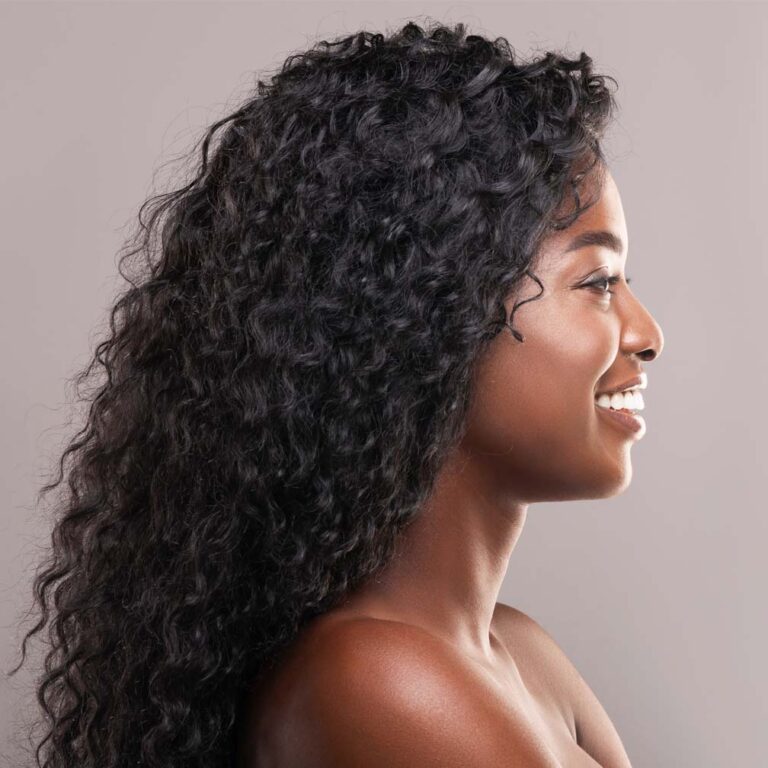 Young model with dark skin and moisturized curly hair posing in profile.