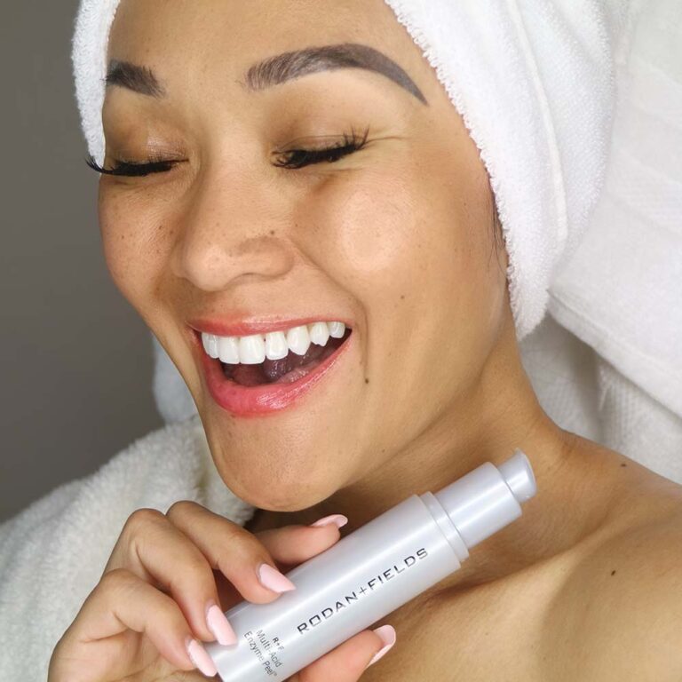 Young woman with gold toned skin pictured with hair towel and eyes closed, holding Rodan + Fields Multi-Acid Enzyme Peel