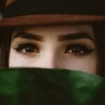 Young woman with strong eyelashes and brows wearing a hat with face obscured by foreground. Photo by Allef Vinicius