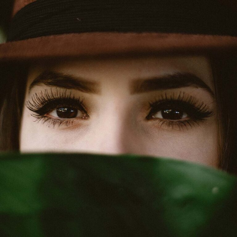 Young woman with strong eyelashes and brows wearing a hat with face obscured by foreground. Photo by Allef Vinicius