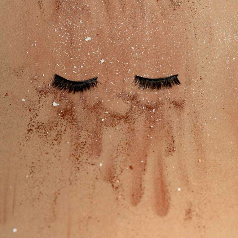 Abstract artwork with two eyelash extensions against a dry textured paper background with makeup debris. Photo by Kier in Sight Archives.