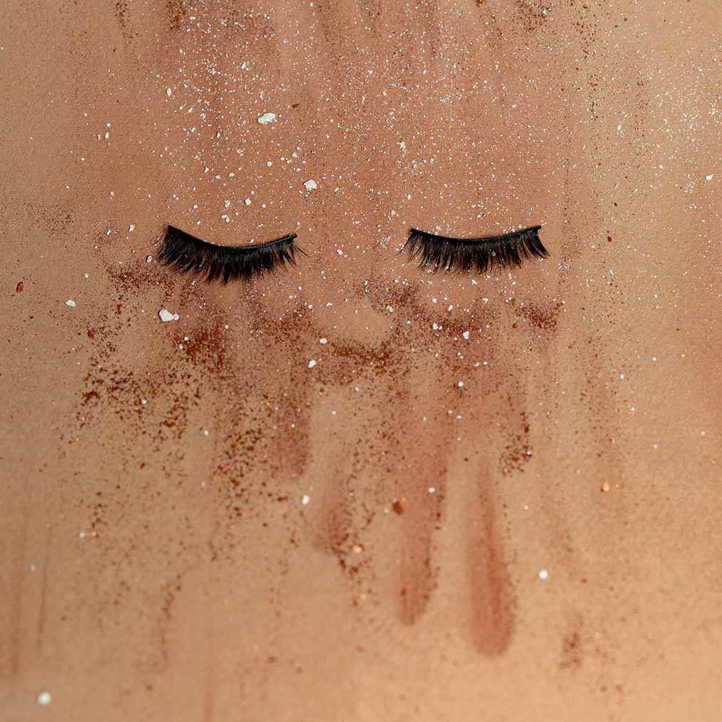 Abstract artwork with two eyelash extensions against a dry textured paper background with makeup debris. Photo by Kier in Sight Archives.
